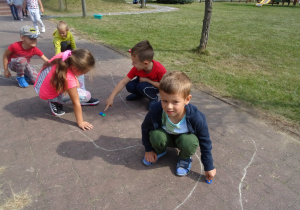 grupka dzieci gra w kapselki i pstryka je po wyznaczonym torze